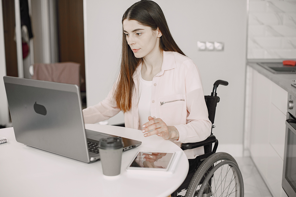 Mujer en silla de ruedas trabajando en su casa con un portátil