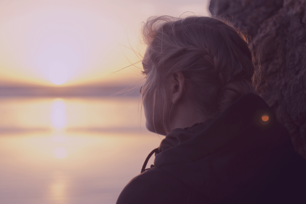 Mujer mirando al horizonte frente al mar en un atardecer