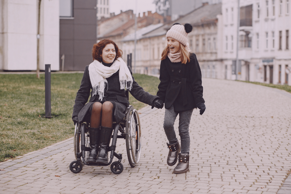 Madre con discapacidad e hija andando por la calle en silla de ruedas