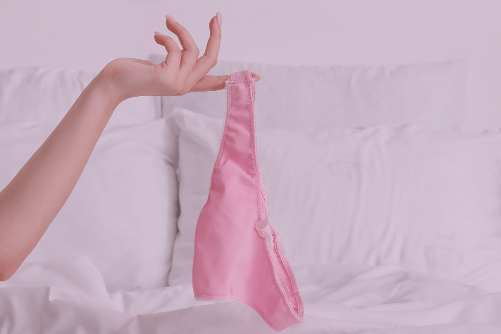 Mano de mujer sujetando unas bragas encima de una cama