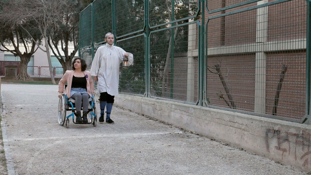 mujer con discapacidad en silla de ruedas caminando junto a un hombre vestido de fantasma con un candil por la calle