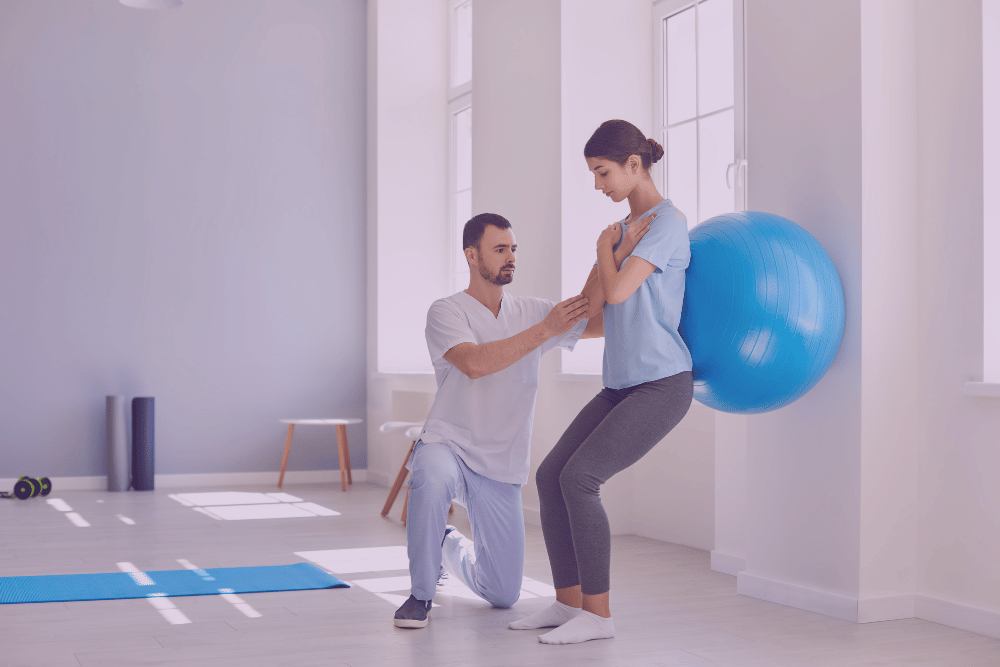 Mujer apoyada en una pelota de gimnasio siguiendo las pautas de un fisioterapeuta