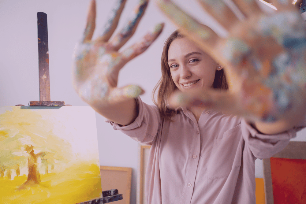 Imagen de mujer con las manos manchadas de pintura con un lienzo pintado a su lado